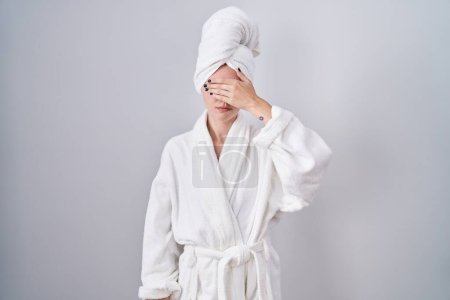 Photo for Blonde caucasian woman wearing bathrobe covering eyes with hand, looking serious and sad. sightless, hiding and rejection concept - Royalty Free Image