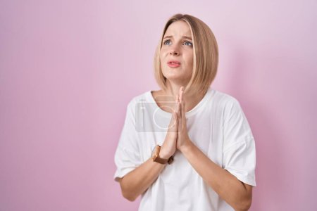 Foto de Young caucasian woman standing over pink background begging and praying with hands together with hope expression on face very emotional and worried. begging. - Imagen libre de derechos