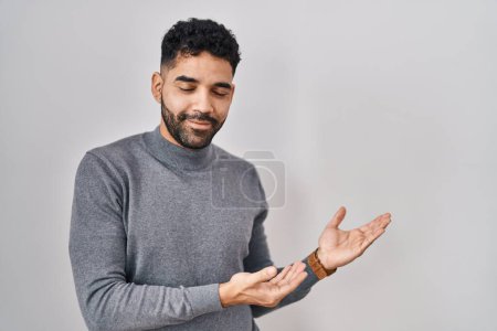 Foto de Hispanic man with beard standing over white background inviting to enter smiling natural with open hand - Imagen libre de derechos