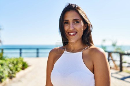 Foto de Joven mujer hispana sonriendo confiada caminando a la orilla del mar - Imagen libre de derechos