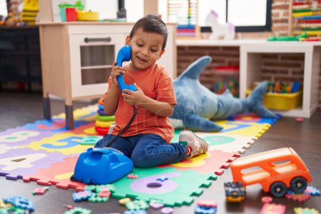 Photo for Adorable hispanic toddler smiling confident sitting on floor playing with telephone toy at kindergarten - Royalty Free Image
