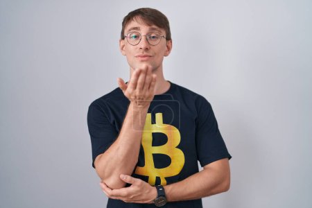 Téléchargez les photos : Caucasian blond man wearing bitcoin t shirt looking at the camera blowing a kiss with hand on air being lovely and sexy. love expression. - en image libre de droit