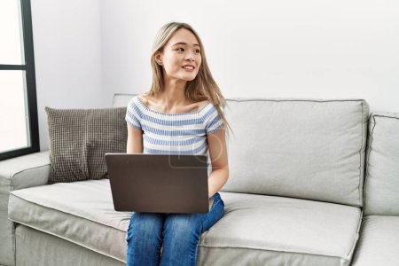 Téléchargez les photos : Jeune femme chinoise souriant confiant en utilisant un ordinateur portable à la maison - en image libre de droit