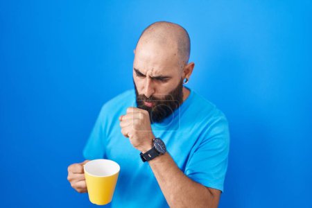 Foto de Joven hispano con barba y tatuajes bebiendo una taza de café sintiéndose mal y tosiendo como síntoma de resfriado o bronquitis. concepto de atención sanitaria. - Imagen libre de derechos