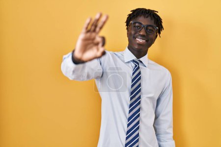 Foto de African man with dreadlocks standing over yellow background smiling positive doing ok sign with hand and fingers. successful expression. - Imagen libre de derechos