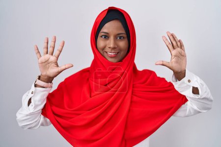 Foto de Young arab woman wearing traditional islamic hijab scarf showing and pointing up with fingers number ten while smiling confident and happy. - Imagen libre de derechos