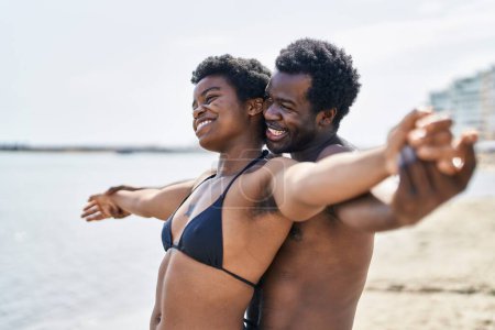 Téléchargez les photos : Couple homme et femme afro-américain en maillot de bain les bras ouverts au bord de la mer - en image libre de droit