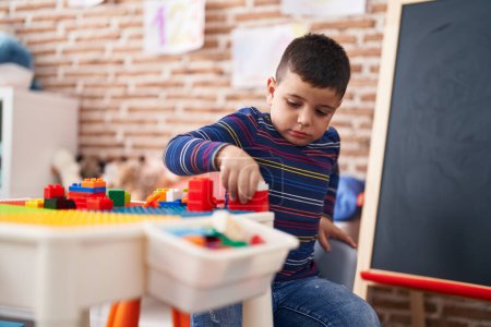 Téléchargez les photos : Adorable hispanic toddler playing with construction blocks sitting on table at kindergarten - en image libre de droit