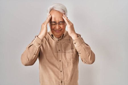Foto de Hombre mayor hispano con gafas que sufren de dolor de cabeza desesperado y estresado porque el dolor y la migraña. manos en la cabeza. - Imagen libre de derechos