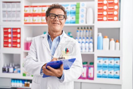 Photo for Middle age man pharmacist smiling confident writing on clipboard at pharmacy - Royalty Free Image