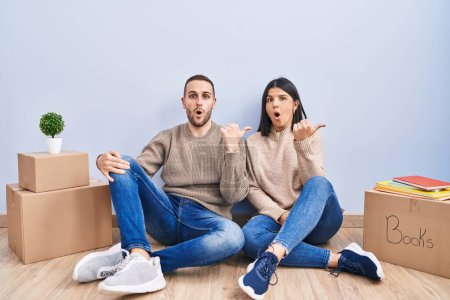 Photo for Young couple moving to a new home surprised pointing with hand finger to the side, open mouth amazed expression. - Royalty Free Image