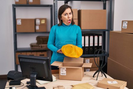 Photo for Middle age hispanic woman working at small business ecommerce preparing order in shock face, looking skeptical and sarcastic, surprised with open mouth - Royalty Free Image