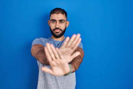 Téléchargez les photos : Moyen-Orient homme avec barbe debout sur fond bleu expression de rejet traversant les bras et les paumes faisant signe négatif, visage en colère - en image libre de droit