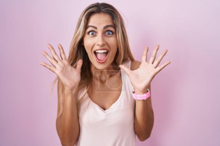 Photo for Young blonde woman standing over pink background celebrating crazy and amazed for success with arms raised and open eyes screaming excited. winner concept - Royalty Free Image
