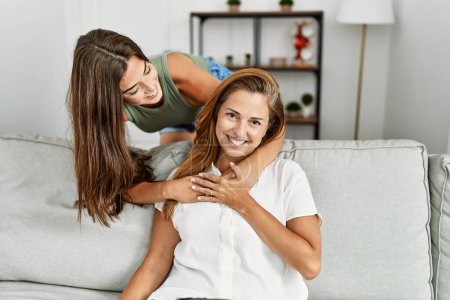 Téléchargez les photos : Mère et fille souriant confiants et s'embrassant assis sur le canapé à la maison - en image libre de droit