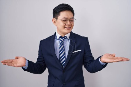 Photo for Young asian man wearing business suit and tie smiling showing both hands open palms, presenting and advertising comparison and balance - Royalty Free Image