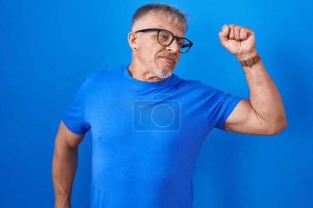 Foto de Hombre hispano con el pelo gris de pie sobre fondo azul que se extiende hacia atrás, cansado y relajado, soñoliento y bostezando por la mañana temprano - Imagen libre de derechos