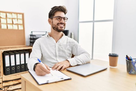 Téléchargez les photos : Jeune homme d'affaires hispanique souriant heureux de travailler au bureau. - en image libre de droit