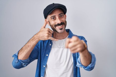 Téléchargez les photos : Homme hispanique avec la barbe debout sur fond isolé souriant faire parler au téléphone geste et vous pointant du doigt. Appelle-moi. - en image libre de droit