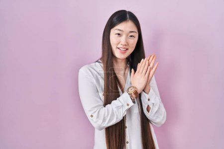Téléchargez les photos : Chinois jeune femme debout sur fond rose applaudissements et applaudissements heureux et joyeux, souriant mains fières ensemble - en image libre de droit