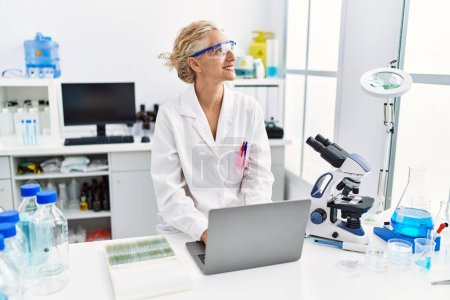 Téléchargez les photos : Femme blonde d'âge moyen portant un uniforme de scientifique travaillant au laboratoire - en image libre de droit