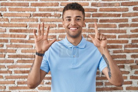 Photo for Brazilian young man standing over brick wall showing and pointing up with fingers number seven while smiling confident and happy. - Royalty Free Image