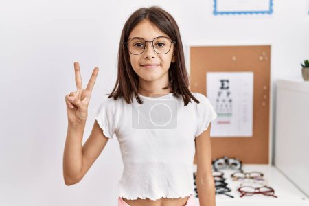 Téléchargez les photos : Jeune fille hispanique portant des lunettes montrant et pointant vers le haut avec les doigts numéro deux tout en souriant confiant et heureux. - en image libre de droit