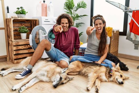 Téléchargez les photos : Jeune couple hispanique faisant la lessive avec des chiens pointant mécontent et frustré à la caméra, en colère et furieux contre vous - en image libre de droit
