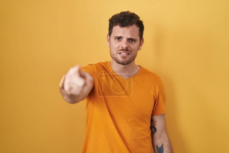 Photo for Young hispanic man standing over yellow background pointing displeased and frustrated to the camera, angry and furious with you - Royalty Free Image