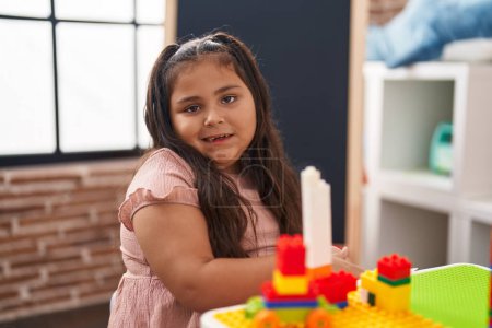 Photo for Plus size hispanic girl playing with construction blocks sitting on table at kindergarten - Royalty Free Image