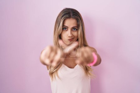 Foto de Joven mujer rubia de pie sobre el fondo rosa expresión de rechazo cruzando los dedos haciendo signo negativo - Imagen libre de derechos
