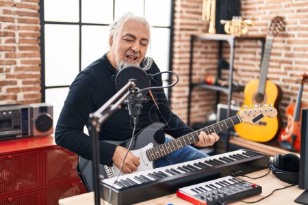 Foto de Músico hombre de pelo gris de mediana edad cantando canción tocando la guitarra eléctrica en el estudio de música - Imagen libre de derechos