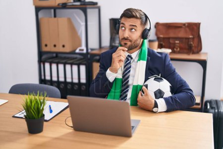 Photo for Handsome hispanic man watching football game at the office serious face thinking about question with hand on chin, thoughtful about confusing idea - Royalty Free Image