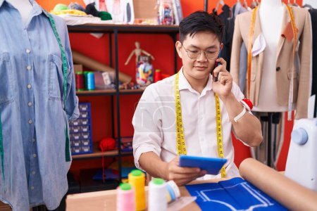 Téléchargez les photos : Young chinese man tailor talking on smartphone using touchpad at atelier - en image libre de droit