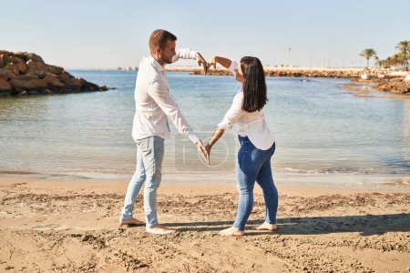 Foto de Hombre y mujer pareja sonriendo feliz haciendo símbolo del corazón con los brazos a la orilla del mar - Imagen libre de derechos