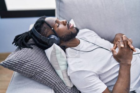Téléchargez les photos : Femme afro-américaine écoutant de la musique détendue sur le canapé à la maison - en image libre de droit