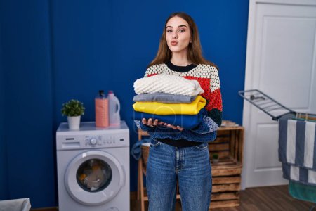 Photo for Young hispanic girl holding clean laundry looking at the camera blowing a kiss being lovely and sexy. love expression. - Royalty Free Image