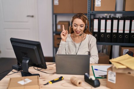 Photo for Hispanic woman working at small business ecommerce wearing headset surprised with an idea or question pointing finger with happy face, number one - Royalty Free Image