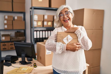 Téléchargez les photos : Middle age woman ecommerce business worker holding package order at office - en image libre de droit