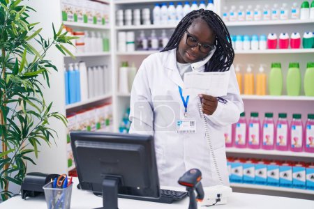 Téléchargez les photos : Pharmacie afro-américaine parlant sur ordonnance de lecture téléphonique à la pharmacie - en image libre de droit