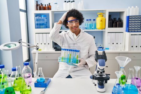 Photo for Hispanic man with curly hair working at scientist laboratory stressed and frustrated with hand on head, surprised and angry face - Royalty Free Image