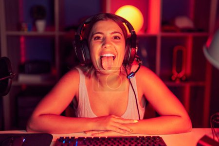 Téléchargez les photos : Young blonde woman playing video games wearing headphones sticking tongue out happy with funny expression. emotion concept. - en image libre de droit