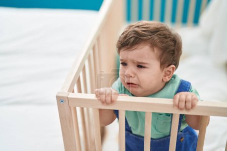 Foto de Adorable niño hispano de pie en la cuna llorando en el dormitorio - Imagen libre de derechos