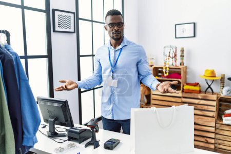 Foto de Joven hombre africano trabajando como gerente en boutique minorista despistado y confundido con los brazos abiertos, sin concepto de idea. - Imagen libre de derechos