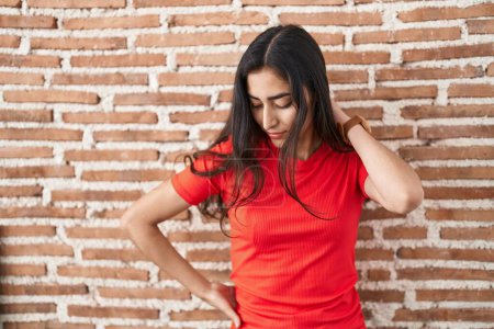 Photo for Young teenager girl standing over bricks wall suffering of neck ache injury, touching neck with hand, muscular pain - Royalty Free Image