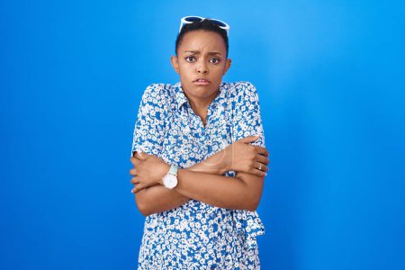 Foto de African american woman standing over blue background shaking and freezing for winter cold with sad and shock expression on face - Imagen libre de derechos