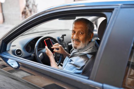 Foto de Hombre de pelo gris senior usando teléfono inteligente sentado en el coche en la calle - Imagen libre de derechos
