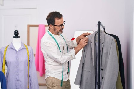 Téléchargez les photos : Homme d'âge moyen tailleur tenant des vêtements sur rack au magasin de tailleur - en image libre de droit