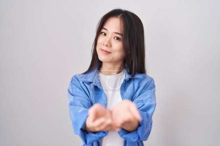 Foto de Joven mujer china de pie sobre fondo blanco sonriendo con las palmas de las manos juntas recibiendo o dando gesto. retención y protección - Imagen libre de derechos