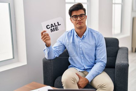 Foto de Hispanic man working at therapy office holding call me banner thinking attitude and sober expression looking self confident - Imagen libre de derechos